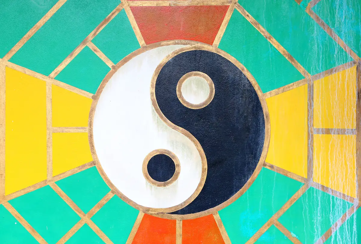 A photo of the ancient chinese Yin Yang sign on a turquoise, yellow, and orange wall of a Chinese temple in Thailand represents Libra's sense of balance and harmony.