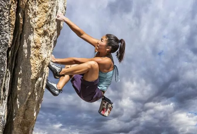 A woman rock climbing in nature with a cloudy sky above.