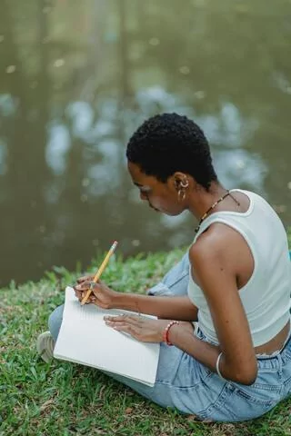 Woman enjoying solitude, writing in journal by a peaceful water.