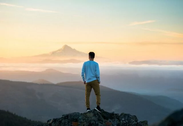 A man alone at the top of a mountain looks out at the sky