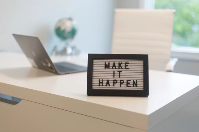 A framed sign on an office desk says, "Make it Happen"