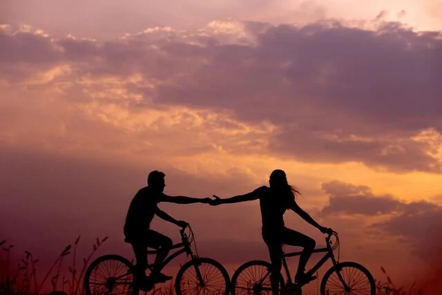Two people holding hands while bicycle riding.