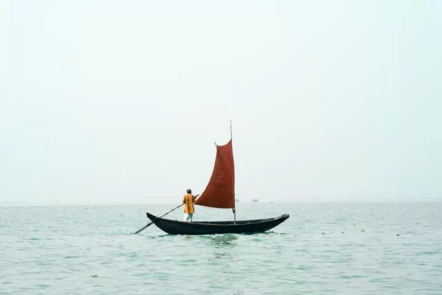 A man on a sailboat on a tranquil sea.