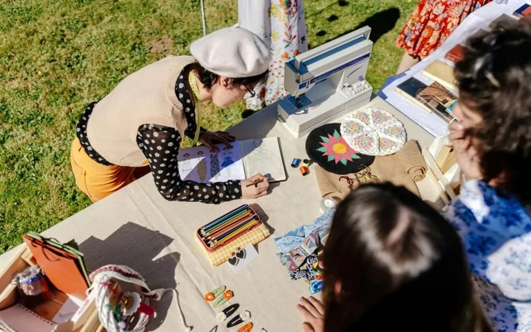 A woman showing her creations at an Art Fair, drawing fashion designs.