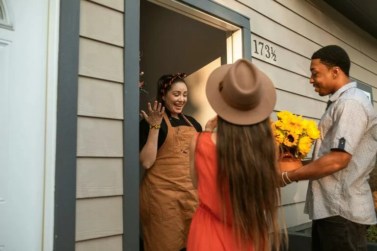 A woman standing on a doorway in front of people bringing flowers