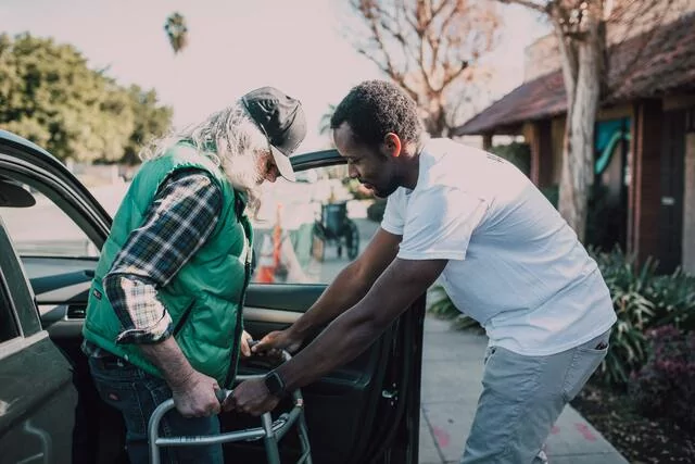 Man helping an elderly man with a walker
